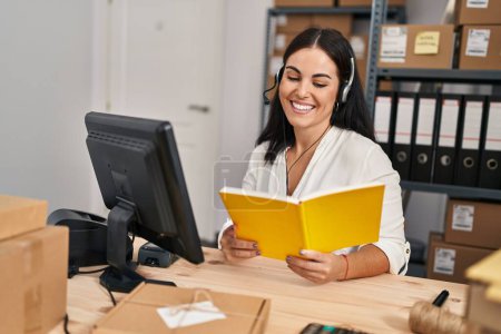 Foto de Joven mujer hispana hermosa comercio electrónico agente de negocios lectura de libro en la oficina - Imagen libre de derechos