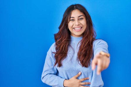 Téléchargez les photos : Hispanic young woman standing over blue background laughing at you, pointing finger to the camera with hand over body, shame expression - en image libre de droit