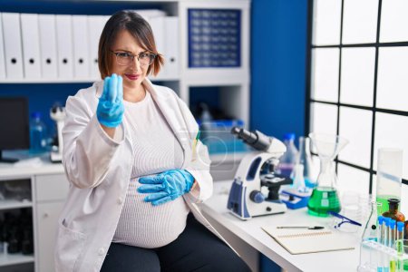 Foto de Pregnant woman working at scientist laboratory doing italian gesture with hand and fingers confident expression - Imagen libre de derechos
