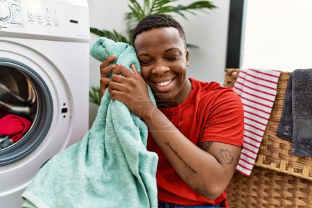 Téléchargez les photos : Jeune homme africain sentir la douceur des serviettes fraîches à la buanderie - en image libre de droit