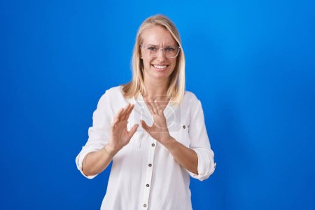 Photo for Young caucasian woman standing over blue background disgusted expression, displeased and fearful doing disgust face because aversion reaction. with hands raised - Royalty Free Image
