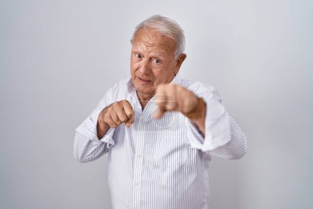 Foto de Hombre mayor con el pelo gris de pie sobre el fondo aislado puñetazo puño para luchar, ataque agresivo y enojado, amenaza y violencia - Imagen libre de derechos