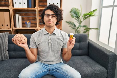 Photo for Hispanic man with curly hair working on depression holding pills relaxed with serious expression on face. simple and natural looking at the camera. - Royalty Free Image