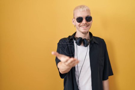 Photo for Young caucasian man wearing sunglasses standing over yellow background smiling cheerful offering palm hand giving assistance and acceptance. - Royalty Free Image