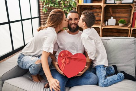Foto de Family kissing father holding heart box gift at home - Imagen libre de derechos