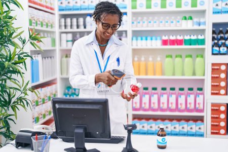 Foto de Middle age african american woman pharmacist scanning pills bottle at pharmacy - Imagen libre de derechos
