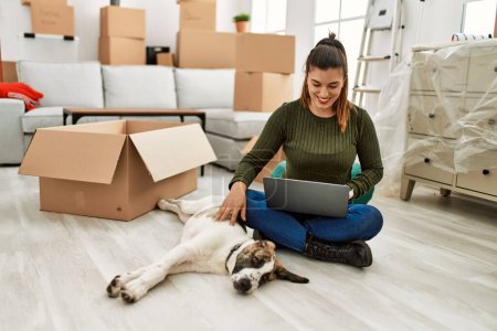 Foto de Mujer joven usando portátil sentado en el suelo con el perro en casa - Imagen libre de derechos