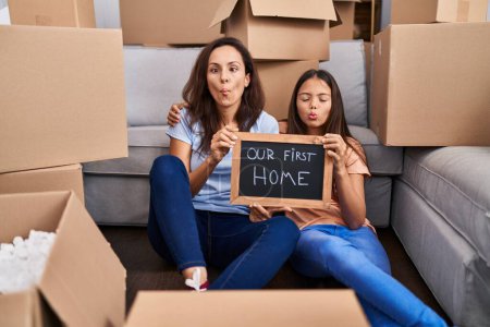 Photo for Young mother and daughter sitting on the floor at new home making fish face with mouth and squinting eyes, crazy and comical. - Royalty Free Image