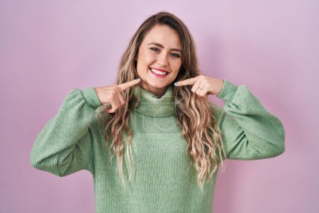 Téléchargez les photos : Jeune femme caucasienne debout sur fond rose souriant joyeuse montrant et pointant avec les doigts dents et la bouche. concept de santé dentaire. - en image libre de droit