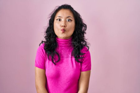 Photo for Young asian woman standing over pink background making fish face with lips, crazy and comical gesture. funny expression. - Royalty Free Image
