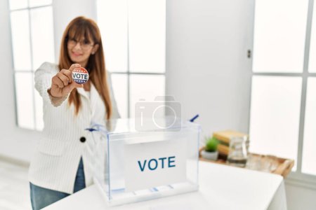 Foto de Joven mujer hispana sonriendo confiada sosteniendo insignia de voto en colegio electoral - Imagen libre de derechos