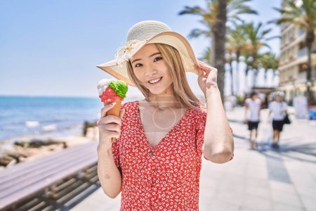 Foto de Joven chica china sonriendo feliz comiendo helado en el paseo marítimo. - Imagen libre de derechos