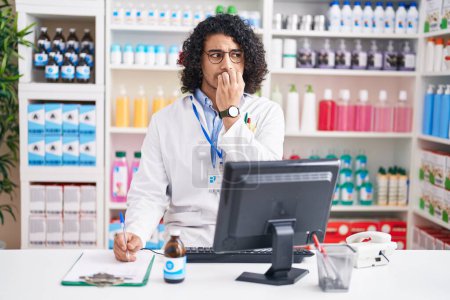Photo for Hispanic man with curly hair working at pharmacy drugstore looking stressed and nervous with hands on mouth biting nails. anxiety problem. - Royalty Free Image