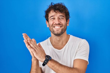 Téléchargez les photos : Jeune homme hispanique debout sur fond bleu applaudissant et applaudissant heureux et joyeux, souriant mains fiers ensemble - en image libre de droit