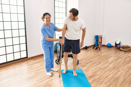 Foto de Hombre y mujer de mediana edad sonriendo confiados en tener sesión de rehabilitación usando bastón para caminar en la clínica de fisioterapia - Imagen libre de derechos