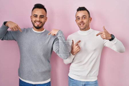Foto de Homosexual couple standing over pink background looking confident with smile on face, pointing oneself with fingers proud and happy. - Imagen libre de derechos