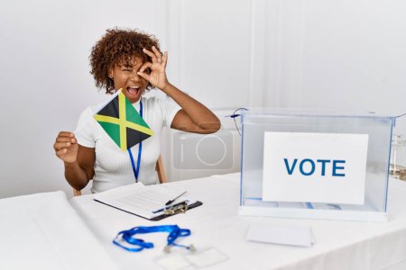 Téléchargez les photos : Young african american woman at political campaign election holding jamaica flag smiling happy doing ok sign with hand on eye looking through fingers - en image libre de droit