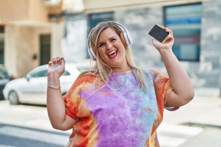 Téléchargez les photos : Jeune femme souriante confiante écoutant de la musique et dansant dans la rue - en image libre de droit