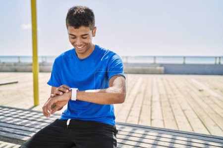 Téléchargez les photos : Jeune homme hispanique formation en utilisant la montre intelligente en plein air - en image libre de droit