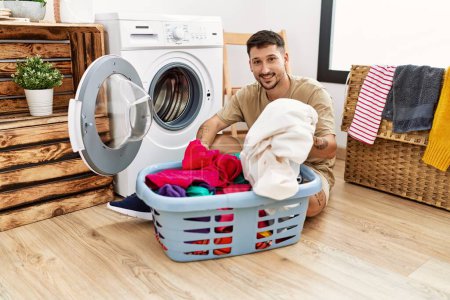 Foto de Joven hombre hispano sonriente confiado usando lavadora en la sala de lavandería - Imagen libre de derechos