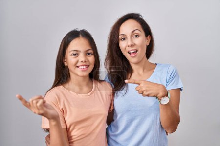 Téléchargez les photos : Young mother and daughter standing over white background with a big smile on face, pointing with hand finger to the side looking at the camera. - en image libre de droit