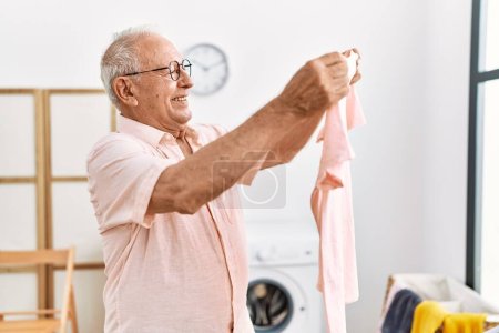 Téléchargez les photos : Senior man holding t shirt hanging clothes on clothesline at laundry room - en image libre de droit