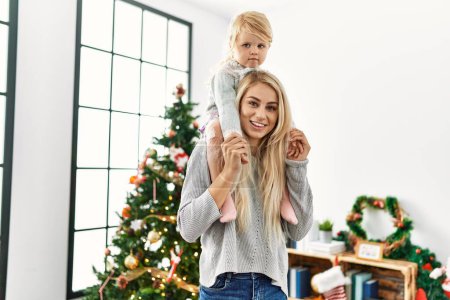 Photo for Mother and daughter holding child on shoulders standing by christmas tree at home - Royalty Free Image