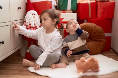 Foto de Brother and sister sitting on floor by christmas gifts at home - Imagen libre de derechos