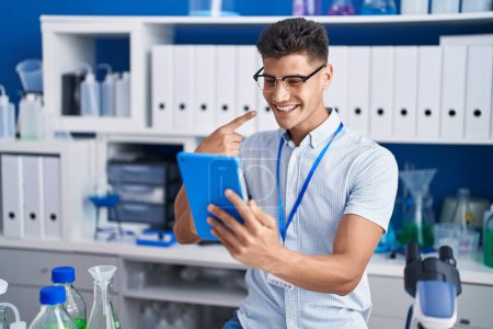 Téléchargez les photos : Jeune homme hispanique travaillant au laboratoire scientifique faire appel vidéo sourire heureux pointant avec la main et le doigt - en image libre de droit