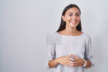 Foto de Mujer hispana joven de pie sobre fondo blanco manos juntas y los dedos cruzados sonriente relajado y alegre. éxito y optimismo - Imagen libre de derechos