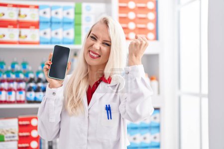 Photo for Caucasian woman working at pharmacy drugstore showing smartphone screen annoyed and frustrated shouting with anger, yelling crazy with anger and hand raised - Royalty Free Image