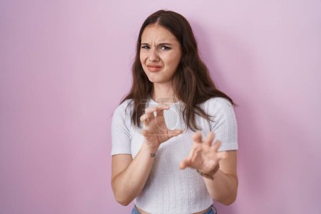 Photo for Young hispanic girl standing over pink background disgusted expression, displeased and fearful doing disgust face because aversion reaction. - Royalty Free Image