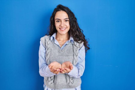 Photo for Young brunette woman standing over blue background smiling with hands palms together receiving or giving gesture. hold and protection - Royalty Free Image