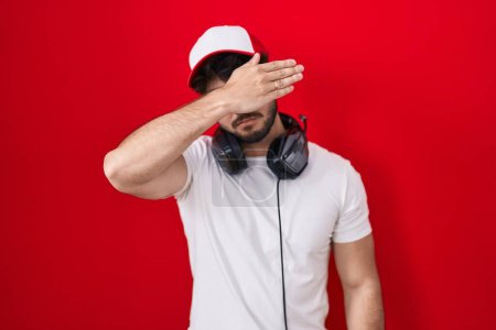 Photo for Hispanic man with beard wearing gamer hat and headphones covering eyes with hand, looking serious and sad. sightless, hiding and rejection concept - Royalty Free Image