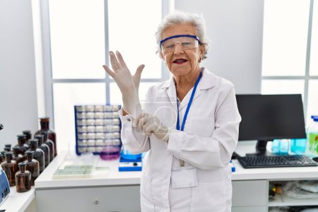Téléchargez les photos : Femme âgée aux cheveux gris portant un uniforme de scientifique portant des gants au laboratoire - en image libre de droit