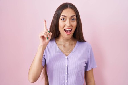 Téléchargez les photos : Jeune femme hispanique avec les cheveux longs debout sur fond rose pointant doigt vers le haut avec idée réussie. Sorti et heureux. numéro un. - en image libre de droit