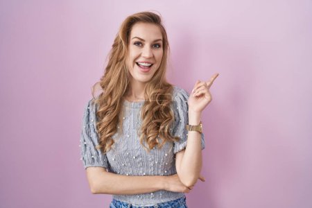 Photo for Beautiful blonde woman standing over pink background with a big smile on face, pointing with hand finger to the side looking at the camera. - Royalty Free Image