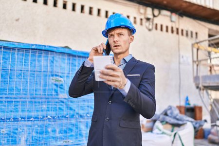Téléchargez les photos : Jeune homme architecte parler sur smartphone lecture ordinateur portable à la rue - en image libre de droit