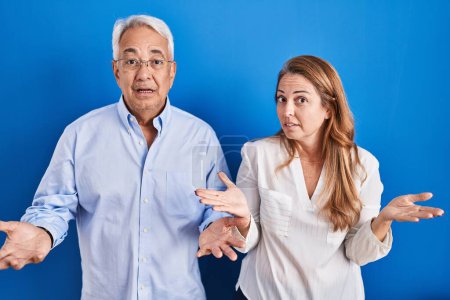 Photo for Middle age hispanic couple standing over blue background clueless and confused with open arms, no idea concept. - Royalty Free Image