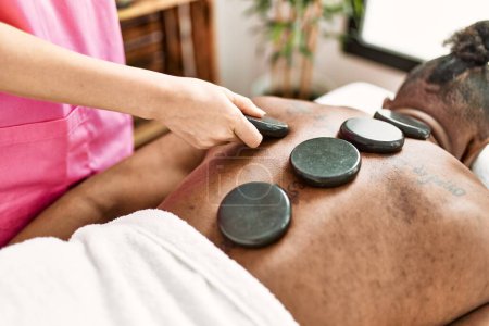 Téléchargez les photos : Jeune homme afro-américain ayant massage du dos avec des pierres chaudes au centre de beauté - en image libre de droit