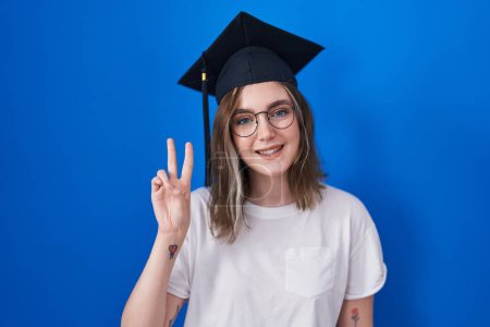 Photo for Blonde caucasian woman wearing graduation cap showing and pointing up with fingers number two while smiling confident and happy. - Royalty Free Image