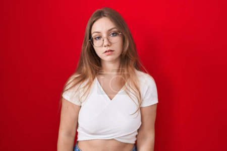 Photo for Young caucasian woman standing over red background looking sleepy and tired, exhausted for fatigue and hangover, lazy eyes in the morning. - Royalty Free Image