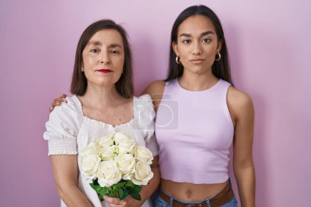 Photo for Hispanic mother and daughter holding bouquet of white flowers relaxed with serious expression on face. simple and natural looking at the camera. - Royalty Free Image