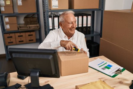 Téléchargez les photos : Senior man ecommerce business worker opening package at office - en image libre de droit