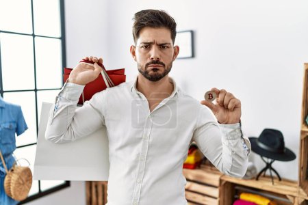 Photo for Young man with beard holding shopping bags and bitcoin skeptic and nervous, frowning upset because of problem. negative person. - Royalty Free Image