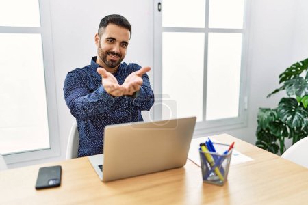 Photo for Young hispanic man with beard working at the office with laptop smiling with hands palms together receiving or giving gesture. hold and protection - Royalty Free Image