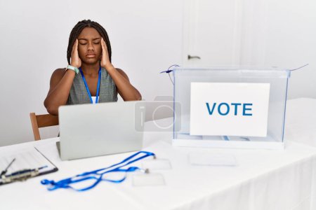 Foto de Mujer afroamericana joven que trabaja en las elecciones políticas sentada por votación con la mano en la cabeza, dolor de cabeza porque el estrés. padecer migraña. - Imagen libre de derechos
