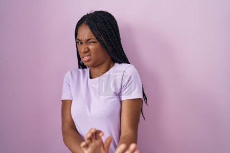Téléchargez les photos : African american woman with braids standing over pink background disgusted expression, displeased and fearful doing disgust face because aversion reaction. - en image libre de droit
