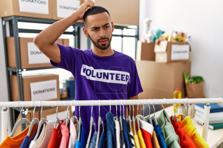Foto de African american man wearing volunteer t shirt at donations stand confuse and wonder about question. uncertain with doubt, thinking with hand on head. pensive concept. - Imagen libre de derechos