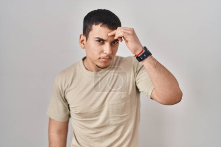Téléchargez les photos : Jeune homme arabe portant t-shirt décontracté pointant malheureux de boutons sur le front, infection laid de la tête noire. acné et problème de peau - en image libre de droit